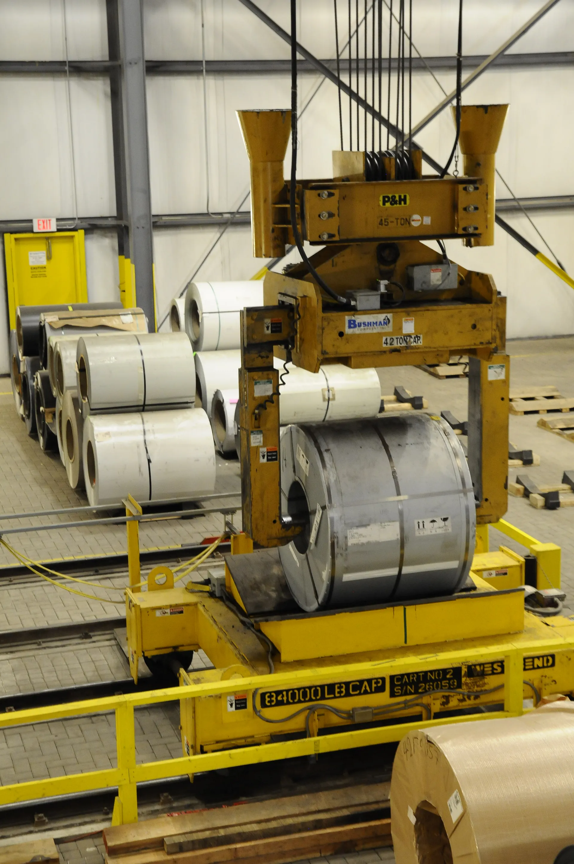 Coil processing line with steel coils, slitters and orange safety railings inside a processing facility